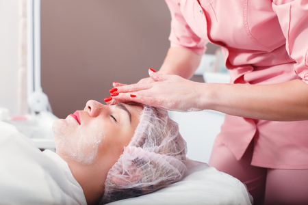 Beautician apply facial cream on young woman face skin. Cosmetic procedure in spa salon. Mask for facial skin careの写真素材