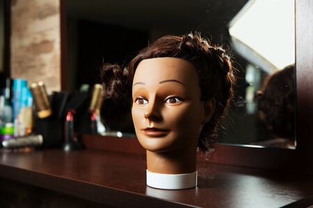 Female hairdressing mannequin is located on a wooden table, hairdressing tools on the background.の写真素材
