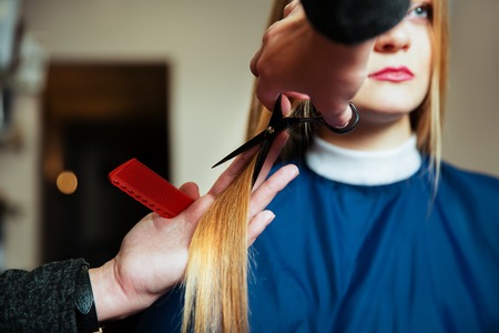 Hairdresser with scissors and comb cute hair to young woman.の写真素材