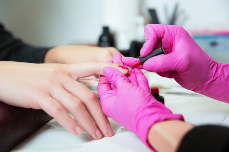 Manicurist in rubber gloves applies a lok on nails. Professional manicure tool.の写真素材