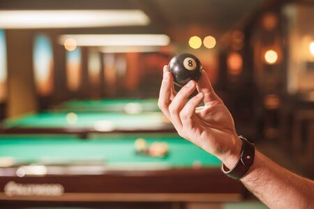 The male hand shows a billiard sphere number eight. Billiard tables on the background.の写真素材