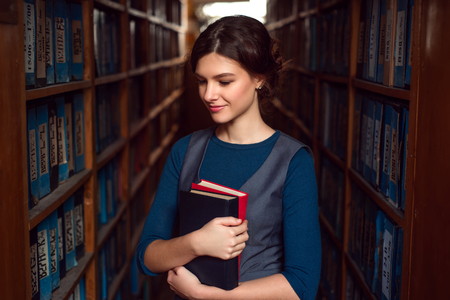 Smiling student girl or woman with books between bookshelves in library.の写真素材
