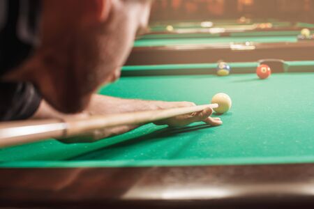 Man trying to hit the ball in billiard. Billiard room on the background.