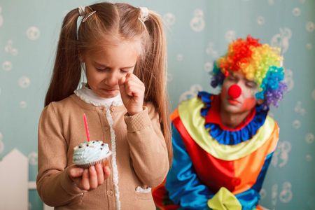 Little girl holding a cake with candle in her hands and crying because she did not have time to make a wish.の写真素材
