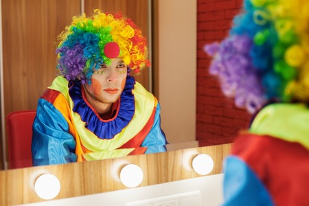 Circus clown looks in a mirror in a make-up room. In waiting of the entertainment.の写真素材