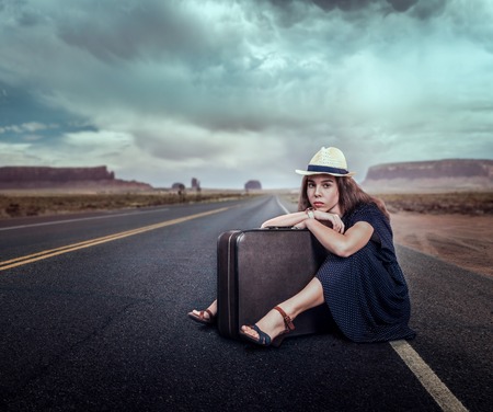 Young girl with luggage traveling hitchhiking. Rocky mountains on the background. Travel concept in retro style.の写真素材