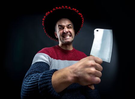 Angry psycho man in pullover and mexican sombrero with meat cleaver on black background. Crazy upset man waiting for his boss.  Office and corporate party concept.の写真素材