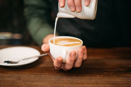 Closeup of male hands adding cream to coffee. Blur table, plate and spoon on the background.の写真素材