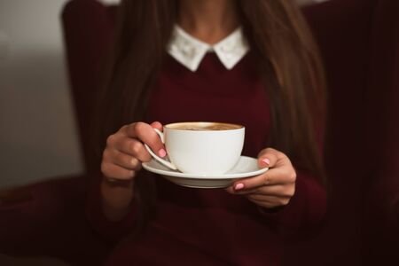 Closeup female hands holding a cup of coffee on saucer.の写真素材