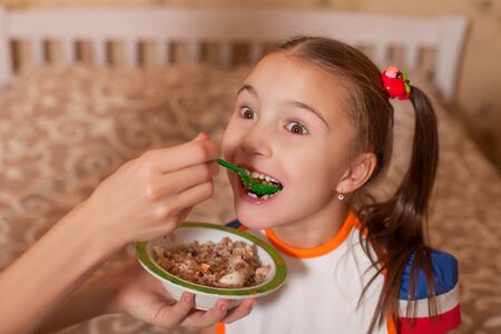 Mothers hand which feeding smiling daughter from a spoon at kitchen.の写真素材