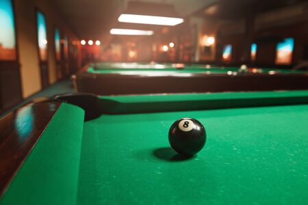 Sphere number 8 opposite to a billiard pocket. Billiard room on the background.