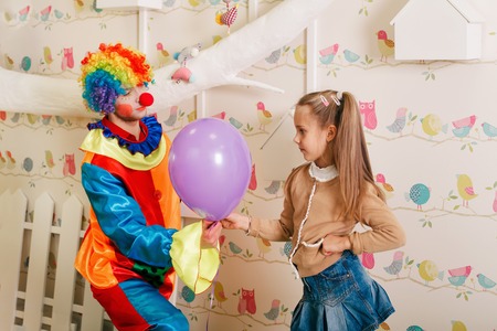 Birthday entertainment with clown in colourful costume. White tree and nesting boxes on the background.の写真素材