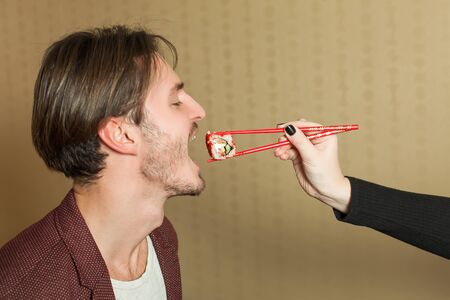 Female hand feeds the man with chopcticks. Japanese food