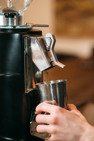 Coffee grinder fills coffee in a cup. Male hand holding a cap near the coffee grinder against blur background.の写真素材
