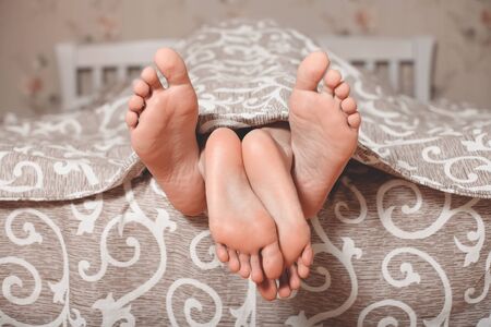 Couple legs stick out from under a blanketの写真素材