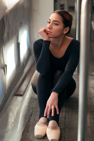 Female ballet dancer sitting against windowの写真素材