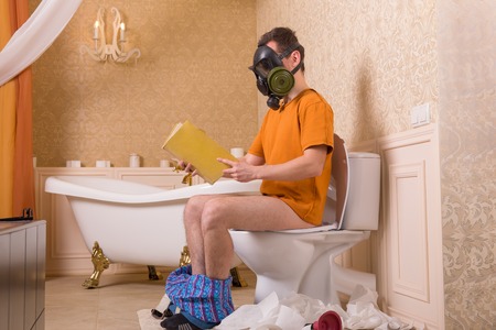 Man in gas mask sitting on toilet and reading bookの写真素材