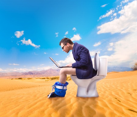 Man with laptop sitting on toilet bowl in desertの写真素材