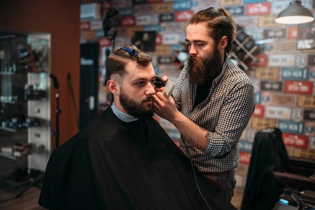 Barber cutting hair of client man in salon capeの写真素材