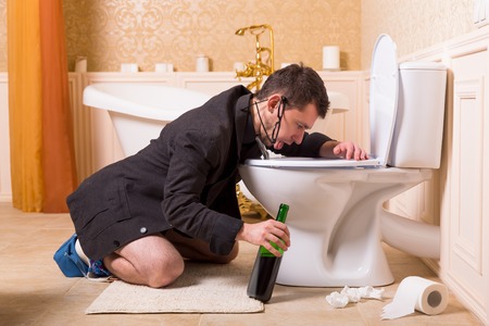 Drunk man with bottle of wine sick in toilet bowl