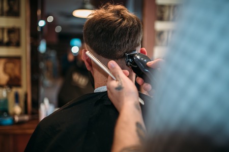 Barber hands makes hairstyle of client by clipperの写真素材