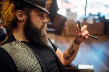 Bearded barber in hat with straight razor in handの写真素材