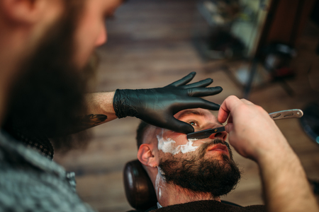 Barber shaves beard of the client at barbershopの写真素材