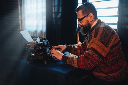 Bearded writer in glasses typing on a typewriterの写真素材