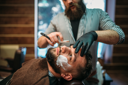 Barber shaves beard of the client at barbershopの写真素材