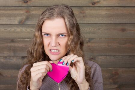 Girl with angry face holding pink heart on a stickの写真素材