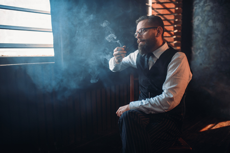 Portrait of man sitting on chair and smoking pipeの写真素材