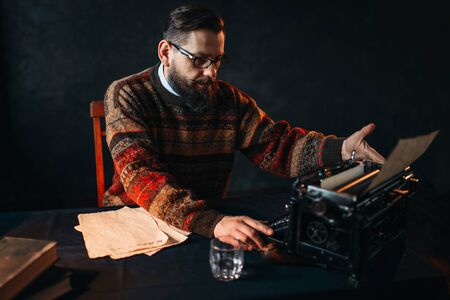 Bearded poet in glasses typing on typewriterの写真素材