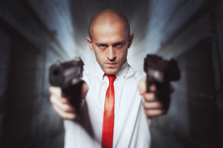 Bald hired killer in red tie aims a pistolsの写真素材