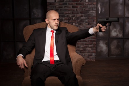 Bald killer in suit and red tie aims a pistolの写真素材