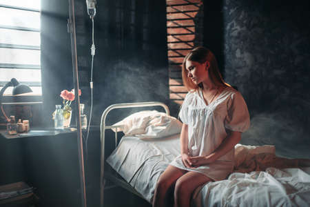Young sick woman sitting on hospital bed on dripの写真素材