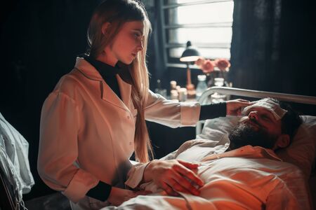 Wife sitting against ill husband in hospital bedの写真素材