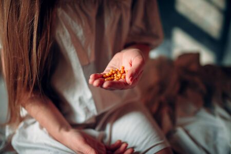 Sick woman sitting on hospital bed, drugs in handの写真素材