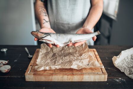Chef hands holds raw fish over cutting boardの写真素材