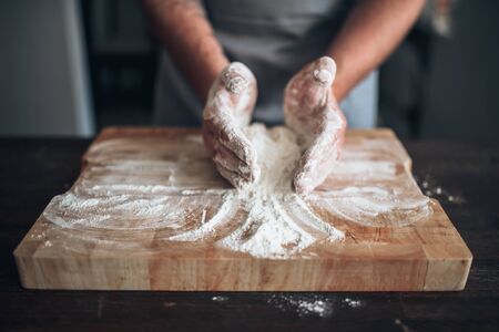 Male baker hands kneading dough on cutting board