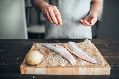 Chef hands salting raw fish over cutting boardの写真素材