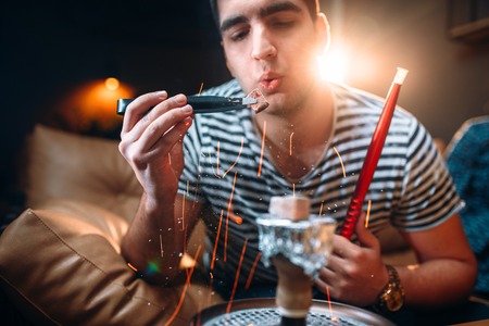 Man holds red-hot coal with tongs, hookah smoking