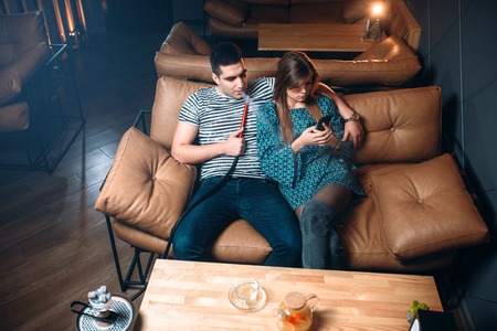 Young couple smoking hookah on leather couchの写真素材
