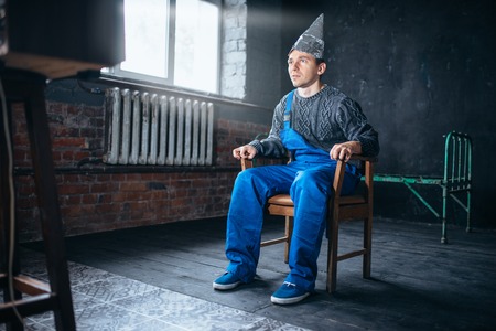 Afraided man in aluminum foil helmet sits in chairの写真素材