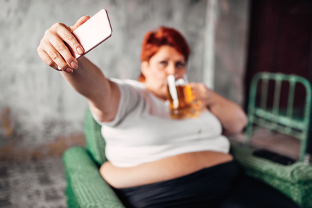 Overweight woman drinks beer and makes selfieの写真素材