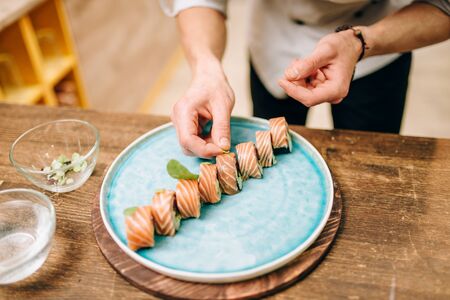 Male person cooking sushi rolls, japanese food