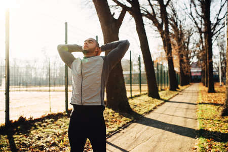 Sportsman warming up before run in autumn park