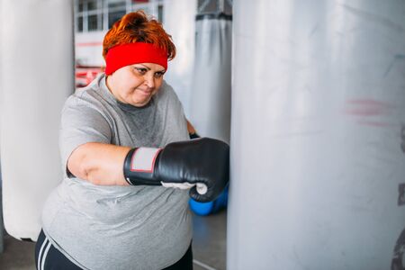 Fat woman in boxing gloves works with punching bagの写真素材