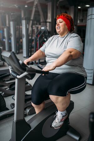 Fat woman training on exercise bike in gymの写真素材