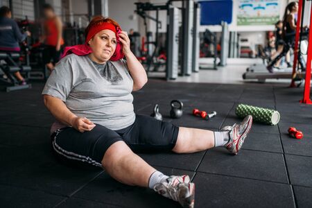 Tired fat woman sits on the floor in gymの写真素材