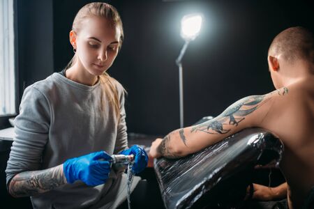 Tattooist makes tattoo by machine on male shoulderの写真素材